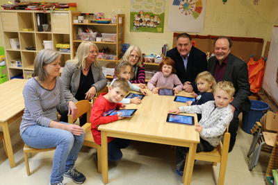 Bild vergr��ern: Louis, Felix, Maliah, Beke und Laura aus der Kita Zwergenburg durften f�r das Foto nur kurz an die Tablets. Denn zun�chst haben nur die Mitarbeiterinnen in den Kitas Zugriff auf die Tablets. Im Hintergrund: (v.l.) Kita-Leiterin Regina Barchfeld, Kita-Leit