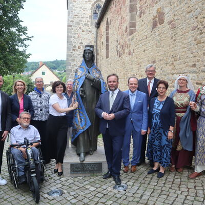 Bild vergr&ouml;&szlig;ern: Eine Gruppe von Menschen steht an einer Skulptur von Kunigunde vor der Stiftskirche in Kaufungen.