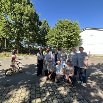 Bild vergr&ouml;&szlig;ern: Auf einem Platz stehen mehrere Frauen zusammen in der Gruppe und blicken in die Kamera. Links neben ihnen fährt ein Kind auf dem Fahrrad.