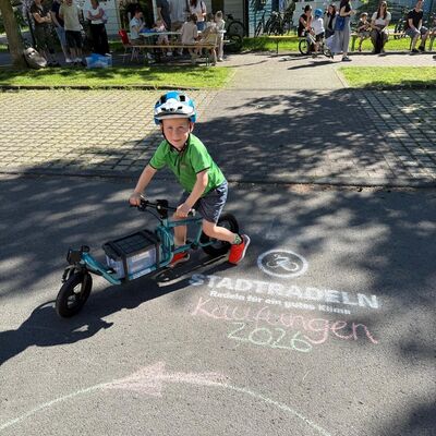 Bild vergr&ouml;&szlig;ern: Ein Kind fährt auf einem kleinen Lastenfahrrad. Vor ihm auf dem Boden vorne im Bild steht mit Kreide "Stadtradeln Kaufungen 2026" geschrieben.