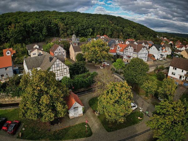 Bild vergr&ouml;&szlig;ern: Eine Luftaufnahme zeigt den Ortsteil Niederkaufungen mit Blick auf die Kirche, Fachwerkhäuser und grüne Bäumen mittendrin.
